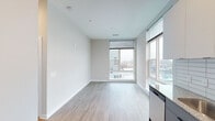 Located at 604 Rigsbee Ave in Durham, NC, this single-floor unit showcases a modern design aesthetic characterized by clean lines, neutral tones, and light-toned hardwood-style flooring throughout. The open living area is brightened by large floor-to-ceiling windows fitted with roller blinds, offering views of the surrounding urban streetscape and allowing abundant natural light to fill the space.

The kitchen is efficiently designed with two-tone cabinetry featuring dark lower cabinets and white upper cabinets, complemented by granite countertops, a subway tile backsplash, and stainless steel appliances including a refrigerator, electric range, microwave, and dishwasher. Recessed lighting and a stainless steel sink complete the functional workspace.

The bedrooms are well-proportioned, each featuring large windows that frame city views and continue the consistent hardwood-style flooring found throughout the unit. The bathroom is finished with matching granite countertops on dark cabinetry, matte black hardware and fixtures, a framed mirror, and a glass-enclosed walk-in shower with white tile surround. The overall ambiance is clean, contemporary, and well-lit, suited to urban living in downtown Durham.