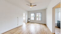This efficient single-floor unit offers a thoughtfully organized layout comprising a bedroom, kitchen, bathroom, closet, and hallway. Light-toned hardwood flooring runs throughout, creating a warm and cohesive aesthetic across all rooms.

The spacious primary bedroom is notably generous relative to the unit's overall footprint, offering ample room for furnishings. Two windows allow natural light to fill the space, while a ceiling fan with a brushed gold fixture provides both style and comfort. A wall-mounted heater sits beneath the windows, and a secondary doorway connects to the hallway for convenient flow.

The galley-style kitchen is outfitted with gray shaker cabinetry, stainless steel appliances including a gas range and full-size refrigerator, and a ventilation hood. Light wood flooring continues seamlessly into this space, and recessed lighting provides functional illumination.

The bathroom features a clean, modern design with a full soaking tub, a gray vanity with a white countertop, brushed nickel fixtures, and a mirror. A frosted window above the tub brings in natural light while maintaining privacy.

The hallway connects all areas efficiently and includes access to a closet fitted with sliding mirrored doors. The entry door is solid white with a clean, minimal design. Throughout the unit, the bright white walls and warm wood floors create a light, airy ambiance.