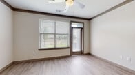This single-floor residence is thoughtfully designed with a cohesive neutral palette and modern finishes throughout. The open-concept living area features light wood-look flooring, crown molding with dark trim accents, and a ceiling fan overhead. A large window paired with a glass-paneled entry door floods the space with natural light and provides views of the surrounding greenery outside.

The kitchen is well-appointed with warm wood cabinetry extending to the ceiling, a white subway tile backsplash, and granite countertops. Stainless steel appliances—including a refrigerator, range, and microwave—are complemented by a kitchen island with an undermount sink and pendant lighting above. An in-unit washer and dryer are conveniently located adjacent to the kitchen.

The bedrooms feature plush carpeting and large windows with outdoor views, creating comfortable, light-filled spaces. Two-panel interior doors in a warm taupe tone add a consistent design element throughout the unit.

The bathroom includes a generous granite vanity countertop with an undermount sink, dark-framed mirror, and wood-toned cabinetry providing ample storage. A walk-in closet with multi-tiered wire shelving offers substantial storage capacity, completing this well-organized and functional residence.