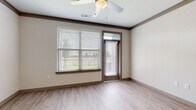 This single-floor residence is thoughtfully designed with a cohesive neutral palette and modern finishes throughout. The open-concept living area features light wood-look flooring, crown molding with dark trim accents, and a ceiling fan overhead. A large window paired with a glass-paneled entry door floods the space with natural light and provides views of the surrounding greenery outside.

The kitchen is well-appointed with warm wood cabinetry extending to the ceiling, a white subway tile backsplash, and granite countertops. Stainless steel appliances—including a refrigerator, range, and microwave—are complemented by a kitchen island with an undermount sink and pendant lighting above. An in-unit washer and dryer are conveniently located adjacent to the kitchen.

The bedrooms feature plush carpeting and large windows with outdoor views, creating comfortable, light-filled spaces. Two-panel interior doors in a warm taupe tone add a consistent design element throughout the unit.

The bathroom includes a generous granite vanity countertop with an undermount sink, dark-framed mirror, and wood-toned cabinetry providing ample storage. A walk-in closet with multi-tiered wire shelving offers substantial storage capacity, completing this well-organized and functional residence.