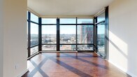 Located in Silver Spring, Maryland, this contemporary high-rise unit offers an impressive blend of modern design and urban convenience. The open-concept living area is defined by expansive floor-to-ceiling windows that wrap around the corner of the space, flooding the interior with natural light and framing sweeping panoramic views of the Silver Spring skyline. Rich hardwood flooring runs throughout the main living areas, adding warmth and elegance to the modern aesthetic.

The kitchen is thoughtfully designed with dark espresso cabinetry, granite countertops, a classic white subway tile backsplash, and a full suite of stainless steel appliances. A central island with a granite countertop provides additional prep space and connects seamlessly to the living area, making it ideal for both cooking and entertaining.

The bedrooms feature plush carpeting and large windows that continue the theme of abundant natural light and city views, with one bedroom offering direct access to a private balcony. The bathrooms are finished with coordinating dark cabinetry and granite countertops; the primary bath features a dual-sink vanity with a wide mirror and elegant fixtures, while the secondary bath mirrors the same refined style. This unit delivers a polished, urban living experience in a prime Silver Spring location.