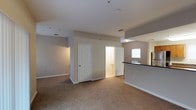 This two-floor residential space offers a clean, functional layout designed for comfortable everyday living. The interior is finished in soft, neutral tones throughout, with warm beige carpeting underfoot that adds a sense of coziness to the living areas. White six-panel doors provide classic detailing and open to adjoining rooms, including a well-placed bathroom that is conveniently accessible from the main living space. The walls are painted in a light greige palette, creating a calm and cohesive atmosphere across the home. A partial wall with a dark countertop edge suggests a kitchen area nearby, hinting at an open or semi-open floor plan that connects the kitchen to the main living area. Recessed ceiling fixtures and HVAC vents are integrated neatly into the ceiling, contributing to a tidy, uncluttered overhead appearance. A window allows natural light to filter into the space, brightening the interior. The layout is practical and straightforward, with clear sightlines across the main level. The second floor adds additional living or sleeping space, making this a versatile multi-level home suited for a range of occupants.