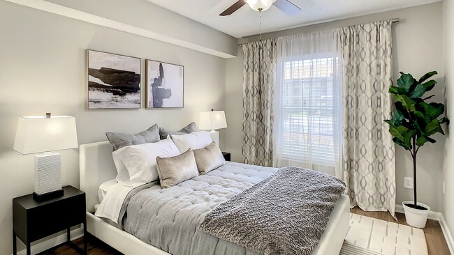 Discover serenity in our spacious bedroom with ceiling fan comfort and expansive sunlit windows. - Adele Place