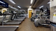 Located at 402 N 18th St in Richmond, Virginia, this fitness center offers a well-equipped, single-floor workout facility designed to support a full range of exercise routines. The space is thoughtfully organized into distinct zones for cardio and strength training, maximizing functionality and ease of movement throughout.

The cardio area is lined with multiple treadmills, elliptical trainers, and stationary bikes, all positioned along floor-to-ceiling mirrors that visually expand the space and allow users to monitor their form. Overhead fluorescent lighting provides bright, even illumination throughout the facility.

The strength-training zone features a cable and pulley multi-station machine, adjustable weight benches, and a well-stocked dumbbell rack spanning a range of weights. Stability balls and additional accessories are available for functional and core-focused training.

Durable carpet tile flooring covers the workout area, offering both comfort and traction underfoot. Exposed architectural elements, including a textured concrete column, add an industrial character to the interior. Large mirrored walls throughout the facility enhance the sense of openness and depth.

The space includes a dedicated exit and connects to adjacent areas via glass-paneled partitions. Overall, the fitness center provides a practical, well-maintained environment suited to a variety of fitness needs and training styles.