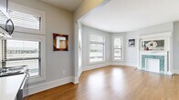 Located at 1506 Laurel Ave in Minneapolis's Lowry Hill neighborhood, this well-appointed one-bedroom, one-bathroom unit offers a thoughtfully designed layout across a single floor. Warm hardwood flooring flows throughout the main living areas, complementing the soft gray walls and crisp white trim that give the space a clean, cohesive aesthetic.

The living room is a standout, anchored by a charming decorative fireplace with an ornate white mantel and distinctive teal tilework, adding a touch of classic character. A curved bay window arrangement floods the space with natural light and provides pleasant views of the surrounding neighborhood.

The kitchen is efficiently designed and stylishly appointed, featuring gray cabinetry, white subway tile backsplash, and a full suite of stainless steel appliances, including a range, microwave, and dishwasher. Its open sightline to the living area creates an inviting, connected feel.

The bedroom is a comfortable retreat, carpeted for warmth, with multiple windows that bring in natural light and offer views of nearby architecture, including a notable domed building. The bathroom is clean and modern, with white subway tile in the walk-in shower, a gray vanity mirror cabinet, and a classic black-and-white striped floor accent. A connecting hallway ties all areas together efficiently.