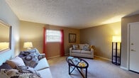 Located at 1825 Liberty Rd in Lexington, Kentucky, this single-floor unit offers a practical and comfortable layout designed for everyday living. The living room serves as the heart of the space, featuring wall-to-wall carpeting, textured ceilings, and warm neutral-toned walls accented by a cool blue feature wall. Natural light filters in through a window dressed with bold red curtains, creating a welcoming ambiance. The open sightlines from the living area connect seamlessly to the hallway and kitchen beyond.

The kitchen is efficiently designed with rich dark wood cabinetry, light countertops, a gas range, and a double-basin sink. Ample upper and lower cabinet storage makes the space highly functional for cooking and meal preparation.

The bedrooms are carpeted and generously sized, each offering natural light through windows with curtain panels. The primary bedroom provides a comfortable retreat with easy access to the kitchen area visible through the doorway.

The bathroom is clean and well-lit, featuring a white vanity with cabinet storage beneath, a lighted mirror above the sink, tile flooring, and a shower-tub combination with a curtain enclosure. Together, these spaces create a cohesive and livable home in a convenient Lexington location.