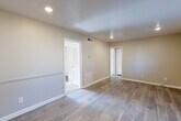 This single-floor residence showcases a clean, modern aesthetic with thoughtfully updated finishes throughout. The open living area is finished with durable wood-look plank flooring and neutral-toned walls, creating a bright and welcoming atmosphere. Recessed lighting illuminates the space, while multiple doorways connect the rooms in a functional and efficient layout. A hallway with a floor-mounted HVAC vent leads seamlessly between the main living spaces. The kitchen stands out as a highlight of the home, featuring crisp white shaker-style cabinetry, a decorative tile backsplash with a mixed stone-and-glass mosaic pattern, stone-look countertops, and black appliances including a refrigerator, electric range, and dishwasher. A window above the sink area brings in natural light. The bedroom offers plush carpeting, a walk-in closet, and a window with blinds that filters in soft natural light. The bathroom is cleanly appointed with wood-look flooring, a tub-shower combination with white tile surround, a vanity, and a toilet. Throughout the home, crisp white trim and baseboards complement the neutral wall palette, contributing to a cohesive and move-in-ready presentation.