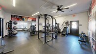 Located at 2190 Ocean Reef Pl in Raleigh, NC, this fitness center spans a single floor and is divided into two exercise rooms, together offering a comprehensive workout environment. The space features durable rubber flooring throughout, providing both safety and comfort during training sessions.

The primary exercise room is appointed with a variety of strength and cardio equipment, including a power rack with weight plates, treadmills, ellipticals, a stair climber, and cable machines. A striking sports-themed mural covers one wall, incorporating bold red and black imagery that energizes the atmosphere. Linear LED lighting runs along the ceiling, complemented by ceiling fans that help maintain air circulation. Large mirrors along the walls enhance the sense of openness and allow users to monitor their form.

The secondary exercise room continues the fitness theme with additional cardio machines, including an Echelon bike and treadmills, along with a full free weight station featuring a dumbbell rack, kettlebells, and a flat bench. Natural light filters in through multiple windows, brightening the space. Glass doors connect the two rooms and provide a view into an adjacent recreation area. The overall aesthetic is clean, modern, and motivational, making this fitness center a fully functional resource for residents.