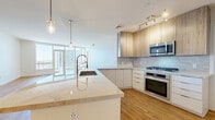 Located in the heart of downtown Phoenix, this modern 1-bedroom, 2-bathroom residence offers a well-designed open-concept layout with warm hardwood-style flooring throughout. The combined kitchen and living area forms the centerpiece of the space, anchored by a generous quartz waterfall island with a sleek commercial-style faucet and undermount sink. The kitchen is equipped with stainless steel appliances, a gas range, built-in microwave, and a full-size side-by-side refrigerator, complemented by a mix of white lower cabinetry and natural wood-toned upper cabinets set against a marble-inspired backsplash. Pendant lighting and track fixtures add a contemporary touch. Floor-to-ceiling windows flood the living area with natural light and open to a private balcony, offering sweeping views of the Phoenix skyline. The spacious bedroom features large corner windows framing additional city views and direct balcony access. Two closets, including a walk-in with built-in shelving, provide ample storage. The primary bathroom impresses with a dual-sink vanity, a soaking tub, and a glass-enclosed walk-in shower finished in neutral tile. An in-unit stacked washer and dryer adds everyday convenience to this polished urban residence.