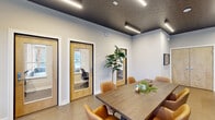 Located at 1340 Wilburn Blvd. in Orbetz, Ohio, this single-story amenity space offers a thoughtfully designed environment that balances collaborative work, private productivity, and social recreation. The layout encompasses several distinct zones, each with its own character and purpose.

The central gathering area features a large wood-top dining or conference table surrounded by cognac leather chairs, positioned beneath a striking dark textured ceiling accented by linear LED lighting fixtures. A foosball table anchors the adjacent game zone, providing a casual recreational outlet within the broader space. Polished concrete flooring flows throughout, lending an industrial-modern aesthetic.

Private offices or focus rooms are accessible through natural wood-framed glass doors, offering quiet, individual workspaces visible from the main area. A darker, more intimate lounge room features matte black walls, cork flooring, a round stone-top table, curated wall art, and a display cabinet — creating a cozy, design-forward retreat.

Additional seating near large windows allows natural light to filter in, providing views of the surrounding exterior. Throughout, the design integrates dark ceilings, light walls, warm furnishings, and contemporary lighting to create a cohesive, modern atmosphere suited for community engagement and focused work alike.