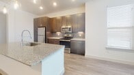 Located at 950 Town Lake Dr in College Station, TX, this well-designed single-floor residence offers a clean, contemporary aesthetic throughout. The open-concept kitchen and living area serves as the heart of the unit, featuring rich dark cabinetry, a gray subway tile backsplash, granite countertops, and a full suite of stainless steel appliances including a refrigerator, range, and microwave. Pendant lighting above the kitchen island adds a stylish touch, while large windows fitted with blinds flood the space with natural light. Wood-look plank flooring extends throughout the main living areas, lending warmth and continuity to the design. The living area is generously proportioned with ample room for comfortable furnishing arrangements. The bedroom is spacious and bright, with recessed lighting and access to a walk-in closet outfitted with dual hanging rods and shelving. The primary bathroom features a granite-topped dark wood vanity, a glass-enclosed walk-in shower with tile surround, and light wood-look flooring. A secondary bathroom includes a soaking tub with tiled surround and a matching granite vanity. Throughout the unit, clean white walls and recessed lighting create a bright, inviting ambiance well-suited to modern living.