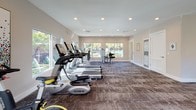 Located at 2770 Roosevelt Blvd in Largo, Florida, this single-floor fitness center is a well-appointed community gym designed to support a comprehensive workout routine. The space is bright and open, with large sliding and fixed windows lining multiple walls, allowing abundant natural light to pour in and offering views of the outdoor pool area and lush Florida landscaping.

The flooring throughout consists of durable, patterned commercial carpet tiles, providing comfort and stability underfoot during exercise. Recessed lighting in the smooth white ceiling supplements the natural light, ensuring the space remains well-lit at all hours.

The cardio section is generously equipped with a row of TRUE-brand treadmills, elliptical trainers, and a stationary cycle, accommodating multiple users simultaneously. A dedicated free weights area features a full rack of dumbbells in varying sizes, accompanied by adjustable benches and a floor-length wall mirror that enhances the sense of space and allows users to monitor their form. Strength and functional training equipment, including a cable machine and a multi-station strength unit, round out the offerings. A functional training corner provides stability balls, medicine balls, and resistance accessories for varied training modalities.

The clean, neutral-toned walls and uncluttered layout create an organized, motivating environment suitable for residents of all fitness levels.