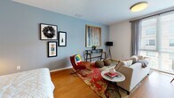 Located at 75 Brainerd Rd in Boston's Allston neighborhood, this modern single-floor studio presents a thoughtfully designed open-concept layout that efficiently combines living, sleeping, and dining areas into one cohesive space. Warm hardwood flooring flows throughout, complementing the clean white walls and contemporary finishes that define the unit's aesthetic.

The kitchen is sleek and fully equipped, featuring dark cabinetry, stainless steel appliances — including a range, microwave, dishwasher, and refrigerator — and a functional countertop workspace. A stacked in-unit washer and dryer is conveniently tucked into an adjacent alcove, adding everyday practicality.

The living area is bright and welcoming, with soft blue-gray walls, room for a full seating arrangement, and space for a dining table. A gallery wall and curated artwork lend the space a vibrant, creative character. The sleeping area integrates seamlessly within the open floor plan, offering a comfortable and private-feeling retreat.

The bathroom is finished with large-format dark tile flooring, a wood-tone vanity with an undermount sink, a frameless mirror, and built-in shelving for additional storage. The overall design is clean and modern, balancing functionality with contemporary style throughout.