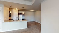 This single-floor residence offers a thoughtfully designed layout that balances open living areas with private retreats. The kitchen serves as a functional centerpiece, outfitted with stainless steel appliances including a refrigerator, electric range, and over-the-range microwave. Rich dark cabinetry contrasts elegantly with granite countertops, while a tile backsplash adds a polished finishing touch. A peninsula with a built-in sink and pendant lighting connects the kitchen to the main living and dining area, which features warm wood-look flooring and flows seamlessly throughout the common spaces. The living room is generously sized, with plush carpeting and a sliding glass door fitted with vertical blinds that invites natural light and provides access to the outdoors. Multiple bedrooms are finished with soft carpeting and feature windows with blinds, offering comfortable, well-lit retreats. Two bathrooms are appointed with dark vanity cabinets, granite countertops, and wood-look flooring; one includes a full tub-shower combination. The neutral color palette and clean lines throughout create a cohesive, modern ambiance suited for comfortable everyday living.