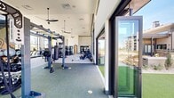 Located at 4692 E Northfield Blvd in Denver's Central Park community, this generously sized fitness center offers a well-rounded workout environment designed to accommodate a wide range of exercise disciplines. The space is defined by soaring ceilings and an abundance of natural light streaming through floor-to-ceiling windows and clerestory glazing, providing open views of the surrounding outdoor amenity areas.

The cardio zone is lined with treadmills, ellipticals, stationary bikes, and rowing machines positioned directly in front of large windows, allowing users to enjoy outdoor views during their workouts. A dedicated strength training area features a full complement of selectorized machines, cable systems, free weights, barbells, and power racks to support comprehensive resistance training. Spin bikes and a striking large-scale fitness-themed mural anchor a dedicated cycling and functional training zone, adding a vibrant visual focal point to the space.

A functional training area is equipped with TRX suspension systems, a punching bag, and battle ropes, while large folding glass doors open directly onto a lush outdoor turf courtyard outfitted with medicine balls, agility equipment, and a shaded pergola. Ceiling fans throughout maintain airflow across the facility. The overall design is modern, clean, and purpose-built to support an active lifestyle.