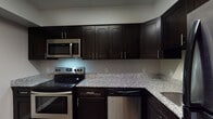 This single-floor residence offers a thoughtfully designed layout that balances functionality and comfort. The kitchen stands as a highlight of the space, showcasing rich, dark espresso-toned shaker-style cabinetry that extends to the upper walls, providing generous storage throughout. Light-speckled granite countertops contrast beautifully against the dark cabinetry, while a full suite of stainless steel appliances — including an electric range, over-the-range microwave, and dishwasher — completes the modern look. Dark hardwood-style flooring anchors the kitchen with a sleek, polished finish.

The bedrooms are carpeted in neutral tones, creating a warm and comfortable atmosphere. Each room benefits from natural light streaming through large windows that offer views of the surrounding neighborhood. Spacious bi-fold closets with built-in rods and shelving provide ample storage in the sleeping areas.

The bathroom features a clean, white tiled tub-shower combination with chrome fixtures and built-in shelving niches, delivering a simple and practical design. Neutral gray walls and white trim carry consistently throughout the space, lending a cohesive and move-in-ready aesthetic. The overall layout, visible in the dollhouse view, reflects an efficient use of space with well-connected living areas.
