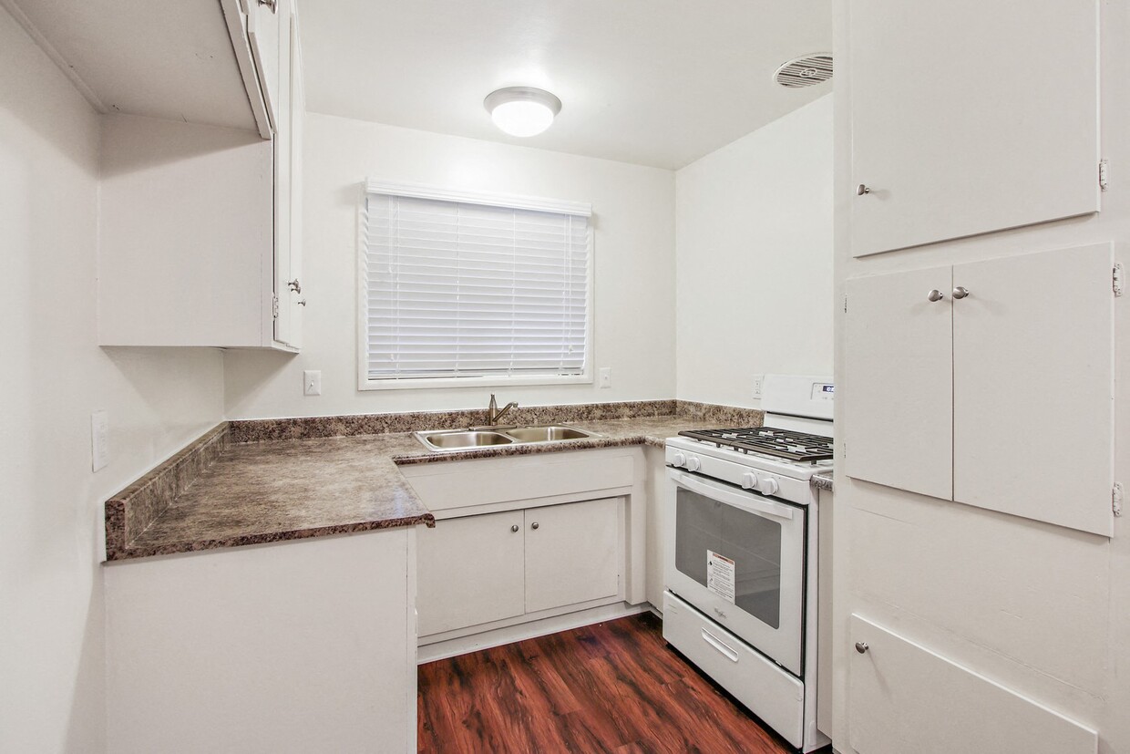 Cocina con encimeras de granito, estufa a gas de color blanco, gabinetes blancos, y pisos de estilo madera - Glen Haven Apartments