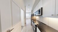 Located at 1465 Lawrence Ave W in Toronto's Lawrence Heights neighbourhood, this efficient one-bedroom, one-bathroom unit is thoughtfully laid out across a single floor. The space features light wood laminate flooring throughout, creating a warm and cohesive aesthetic against the crisp white walls.

The main living and sleeping area is generously proportioned relative to the overall footprint, accommodating a full bedroom setup with a built-in mirrored sliding closet that adds both storage and a sense of depth. A large roller-blind window floods the room with natural light, while a private door provides direct outdoor access — a notable feature for urban living. A wall-mounted split air conditioning unit and a baseboard heater ensure year-round climate comfort.

The kitchen area is positioned near the entrance and is equipped with a stainless steel refrigerator, making practical use of the available space.

The bathroom is finished with clean, white rectangular subway tiles from floor to ceiling, and features a glass-enclosed walk-in shower with chrome fixtures, a toilet, and a minimalist design that emphasizes functionality and cleanliness.

The unit's overall design is modern and neutral, offering a clean canvas well-suited for a range of living arrangements.