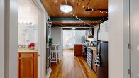 This two-story home in Richmond, Virginia offers a thoughtfully arranged layout across two levels. The main floor hosts a combined living, dining, and kitchen area that maximizes every inch of space. The kitchen is a standout feature, showcasing warm wood cabinetry, granite countertops, black appliances, and a peninsula with bar seating — all beneath a striking natural wood-plank ceiling adorned with globe string lights that lend a cozy, inviting ambiance. Hardwood floors run throughout, adding warmth and continuity between areas. A pantry and in-unit laundry add notable convenience on this level. The upper floor is dedicated to the private bedroom suite, a generously proportioned retreat with gleaming hardwood floors, crisp white walls, and a large closet. The open staircase connects both levels with an airy feel. The full bathroom features tile flooring, warm wood vanity cabinetry, and granite countertops, maintaining a consistent design language throughout the home. Additional closet storage ensures practical living. Located in Richmond's historic Church Hill neighborhood, this two-story home combines efficient, well-planned living spaces with distinctive architectural character.