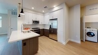 This single-floor unit showcases a thoughtfully designed open-concept layout with modern finishes throughout. The kitchen serves as a central highlight, featuring a two-tone design with crisp white upper cabinetry and rich wood-grain lower cabinets, complemented by quartz countertops, a subway tile backsplash, and a full suite of stainless steel appliances including a gas range, built-in microwave, and French door refrigerator. A kitchen island with pendant lighting adds both functionality and style, flowing seamlessly into the living area. The living space is finished with wood-style flooring and benefits from abundant natural light through multiple windows and a glass door that opens to an outdoor area. Track lighting provides additional illumination. Two bedrooms are finished with plush carpeting, ceiling fans, and windows with outdoor views; each bedroom is accompanied by its own walk-in closet offering built-in shelving. Two bathrooms mirror the unit's contemporary aesthetic, featuring white cabinetry with quartz countertops, framed mirrors, and glass-enclosed showers with wood-style flooring. An in-unit laundry area completes this well-appointed space.