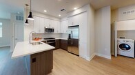 This single-floor unit showcases a thoughtfully designed open-concept layout with modern finishes throughout. The kitchen serves as a central highlight, featuring a two-tone design with crisp white upper cabinetry and rich wood-grain lower cabinets, complemented by quartz countertops, a subway tile backsplash, and a full suite of stainless steel appliances including a gas range, built-in microwave, and French door refrigerator. A kitchen island with pendant lighting adds both functionality and style, flowing seamlessly into the living area. The living space is finished with wood-style flooring and benefits from abundant natural light through multiple windows and a glass door that opens to an outdoor area. Track lighting provides additional illumination. Two bedrooms are finished with plush carpeting, ceiling fans, and windows with outdoor views; each bedroom is accompanied by its own walk-in closet offering built-in shelving. Two bathrooms mirror the unit's contemporary aesthetic, featuring white cabinetry with quartz countertops, framed mirrors, and glass-enclosed showers with wood-style flooring. An in-unit laundry area completes this well-appointed space.