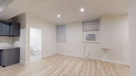 Located at 750 S Mariposa Ave in the heart of Los Angeles' Koreatown neighborhood, this single-floor unit offers a clean, modern interior with consistent light wood laminate flooring throughout. The open living and dining area is bright and airy, illuminated by recessed lighting and natural light from blinds-fitted windows. A wall-mounted air conditioning unit provides climate control. The kitchen is well-appointed with slate gray shaker-style cabinetry, stainless steel appliances including a full-size refrigerator and electric range, a white subway tile backsplash, and a built-in sink — delivering both style and functionality. Two bedrooms offer comfortable layouts; one features a ceiling fan with overhead lighting and dual windows, while the other includes mirrored sliding closet doors that enhance the sense of space. A shared hallway connects the rooms to a full bathroom finished in crisp white, complete with a vanity, mirror, toilet, and a shower/tub combination. The overall design is clean and minimalist, with white walls and consistent finishes that create a cohesive, move-in-ready feel throughout the entire unit.