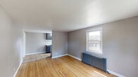 Located at 1310 Nottingham Way in Hamilton, NJ, this one-bedroom, one-bathroom unit offers a thoughtfully arranged layout with a blend of classic charm and modern updates. The combined kitchen and living area serves as the heart of the space, where warm hardwood floors flow throughout and a cast-iron radiator adds a touch of character beneath a bright window overlooking the neighborhood. The kitchen is outfitted with dark cabinetry, white subway tile backsplash, light countertops, and stainless steel appliances including a gas range and refrigerator, with a window that brings in natural light and views of the surrounding greenery. The bedroom features soft carpeting, neutral-toned walls, and a built-in closet with a hanging rod for convenient storage. The bathroom stands out with floor-to-ceiling marble-style tile surrounding a clean white soaking tub and shower combination, complemented by a window that adds ventilation and natural light. A hallway connects the rooms efficiently, with additional closet space along the way. The overall ambiance is clean, functional, and comfortable, making this a practical and well-maintained unit in a residential Hamilton neighborhood.