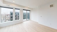 This thoughtfully designed 3-bedroom, 2-bathroom unit offers a clean, contemporary aesthetic throughout its single floor. Light hardwood flooring flows seamlessly across all rooms, creating a bright and cohesive feel. The open living and dining area is highlighted by expansive floor-to-ceiling windows and a sliding glass door that opens onto a private balcony, allowing abundant natural light and views of the surrounding neighborhood. The modern kitchen is well-appointed with flat-front cabinetry in a warm taupe finish, stainless steel appliances including a range, microwave, dishwasher, and refrigerator, complemented by a white subway tile backsplash and ample storage. Each of the three bedrooms features a built-in closet with sliding doors and wire shelving. The bedrooms are served by two clean, minimalist bathrooms — one with a vanity and toilet, and another with a full tub-shower combination. Two hallways efficiently connect the private sleeping quarters to the shared living spaces, maintaining a functional layout. The unit's crisp white walls, recessed lighting, and modern fixtures throughout contribute to a polished, move-in-ready atmosphere suited for contemporary urban living.