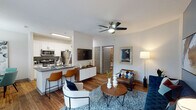 This single-story residence offers a thoughtfully designed open-concept layout that seamlessly connects the living, dining, and kitchen areas. The living room features warm hardwood-style flooring, a ceiling fan, a bold blue accent wall, and sliding glass doors that invite natural light and provide access to an outdoor patio. The kitchen is equipped with stainless steel appliances — including a refrigerator, gas range, and microwave — complemented by crisp white shaker cabinetry, gray countertops, and a breakfast bar with seating. Adjacent to the kitchen, a dedicated dining nook is brightened by a large window and features a pendant light fixture overhead. Both bedrooms are carpeted for comfort, each with ceiling fans, large windows with outdoor views, and distinctive accent walls — one in slate blue and another in teal — creating a calm, contemporary atmosphere. The bathrooms include white vanity cabinetry with gray countertops, framed mirrors, and tub-shower combinations with tiled surrounds. Hardwood-style flooring flows consistently through the main living areas, tying the space together with warmth and cohesion. The overall design balances modern finishes with a welcoming, residential aesthetic.