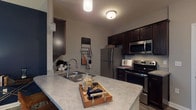 Located at 5260 Franklin St in Hilliard, Ohio, this single-floor residence offers a thoughtfully designed layout with a warm, eclectic character throughout. The kitchen is a functional highlight, featuring dark espresso cabinetry, light stone-look countertops, stainless steel appliances including a refrigerator, electric range, and built-in microwave, as well as wood-look luxury vinyl plank flooring. A peninsula with a double sink provides additional prep space and adds an open, connected feel. Conveniently tucked just off the kitchen is an in-unit laundry area with a full-size washer and dryer. The living room makes a bold statement with deep navy accent walls, hardwood-style flooring, and large windows that invite natural light. It offers generous space for seating and entertainment. The bedrooms are carpeted and comfortably sized, each with its own distinct character — one features a rustic barn door headboard detail, while another benefits from a bright window with pleasant outdoor views. The full bathroom is finished with vinyl plank flooring, a dark vanity with a single sink, and a shower-tub combination. Overall, the space blends modern finishes with warm, rustic accents to create an inviting and functional home.