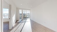 Located at 1502 S Fawcett Ave in Tacoma, WA, this thoughtfully designed one-bedroom, one-bathroom unit delivers a clean, modern aesthetic across a well-utilized single floor. Light hardwood-style flooring runs throughout, complementing the bright white walls and creating a cohesive, contemporary feel.

The kitchen is a standout feature, showcasing two-tone cabinetry that pairs warm wood uppers with weathered gray lower cabinets, set against classic white subway tile backsplash. Dark quartz countertops extend across an L-shaped peninsula with pendant lighting overhead, providing both prep space and a casual dining area. Stainless steel appliances, including a refrigerator, range, and microwave, complete the space.

The living room is filled with natural light streaming through large floor-to-ceiling sliding glass doors that open directly onto a private balcony with outdoor views. The bedroom offers a tranquil retreat with generous closet storage via sliding doors and sun-drenched natural light. A versatile den provides additional flexible living space.

The bathroom features a dark-toned vanity with a black quartz countertop, undermount sink, and a large mirror with modern sconce lighting. In-unit laundry adds everyday convenience, rounding out this well-appointed Tacoma residence.