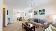 Located on Sugar Maple Loop N in Huber Heights, Ohio, this single-floor residence offers a thoughtfully designed layout that balances comfort and functionality. The open-concept living and dining area serves as the heart of the home, featuring neutral-toned carpet, bright white walls, and multiple windows that invite generous natural light throughout. A ceiling fan with a light fixture anchors the living space, which flows seamlessly into a dedicated dining area illuminated by an elegant chandelier pendant.

The galley-style kitchen is well-equipped, featuring warm wood cabinetry with ample storage, light-toned countertops, a double sink, and white appliances including a range and refrigerator. Stone-look tile flooring adds a practical and polished finish to this area.

The bedroom is generously proportioned, with plush carpeting, a large window dressed with decorative curtains, and sufficient space for substantial furnishings. Framed artwork above the bed enhances the room's comfortable ambiance.

The bathroom features the same tile flooring as the kitchen and includes rich wood cabinetry beneath a light countertop, providing practical storage. The layout is clean and efficiently arranged. Overall, the residence presents a cohesive, well-lit interior with a warm, livable character throughout.