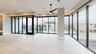 This contemporary 3-bedroom, 2-bathroom residence is thoughtfully designed with modern finishes and an open, functional layout across a single floor. The living area is a standout feature, boasting expansive floor-to-ceiling windows and glass doors that frame sweeping city skyline views, flooding the space with natural light. A ceiling fan anchors the room, and direct access to the private balcony makes indoor-outdoor living seamless.

The kitchen is a chef-inspired space featuring a large central island with a quartz countertop and integrated sink, complemented by two-tone cabinetry combining rich walnut-toned wood with crisp white uppers. Stainless steel appliances, pendant lighting, and recessed fixtures complete the polished look.

A well-lit hallway connects the bedrooms, lined with distinctive dark wood doors with matte black hardware. The primary bedroom offers its own balcony access with city views and a modern ceiling fan. Additional bedrooms feature patterned carpet flooring and generous closet storage.

The primary bathroom includes a double-sink vanity with backlit mirrors, wood-toned cabinetry, and a glass-enclosed shower. The second bathroom offers a clean, neutral palette with a soaking tub, vessel sink, and light tile flooring. In-unit laundry adds further convenience to this well-appointed urban residence.