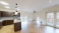 This single-floor unit showcases a thoughtfully designed open layout that seamlessly connects the kitchen and living areas. The herringbone-patterned hardwood flooring flows throughout the main living spaces, creating a visually striking foundation that enhances the overall aesthetic. Multiple windows dressed with roller shades invite generous natural light while offering views of the surrounding urban environment.

The kitchen is well-appointed with dark espresso cabinetry, granite countertops, a tile backsplash, and a full suite of stainless steel appliances including a refrigerator, range, microwave, and dishwasher. A central island provides additional prep space and seating, while pendant lighting adds a modern touch overhead. Ceiling fans are featured in both the living area and bedrooms.

The bedrooms offer a comfortable retreat, with plush carpeting in the primary sleeping areas and ample natural light through large windows. Additional rooms with herringbone flooring provide flexible living or dining space.

The bathrooms are finished with decorative patterned tile flooring, dark espresso vanities topped with granite countertops, matte black fixtures, and white tiled tub/shower combinations, delivering a clean, contemporary feel throughout.