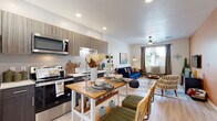 This thoughtfully designed single-floor residence offers a seamless open-concept layout that connects the kitchen and living area into one cohesive, functional space. The kitchen is outfitted with stainless steel appliances — including a refrigerator, electric range, over-the-range microwave, and dishwasher — complemented by two-tone cabinetry in dark wood and light gray finishes, white countertops, and light wood-style flooring that flows throughout the common areas. Recessed lighting and natural light from blinds-fitted windows keep the space bright and welcoming.

The living area features a warm accent wall in a rich terracotta tone, a ceiling fan, and a window with outdoor views, creating a comfortable and inviting retreat. The bedroom continues the warm color palette with a bold accent wall, plush carpet flooring, a ceiling fan, and generous natural light through curtained windows.

The bathroom is cleanly finished with a wood-toned vanity, white countertop, oval mirror with Hollywood-style lighting, and a tub-shower combination. A dedicated utility nook houses a full-size stacked washer and dryer alongside a built-in wall desk, adding practical functionality to the home's efficient use of space.