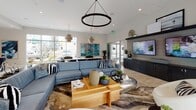 Located at 1902 Millenia Ave in Chula Vista, CA, this single-floor community clubhouse offers a thoughtfully designed open-plan layout that seamlessly blends comfort, style, and functionality. The main lounge area is anchored by a generous sectional sofa in a cool blue hue, complemented by a bold circular pendant light and a wall-mounted flat-screen TV set against dark cabinetry. Light wood-look flooring runs throughout, lending warmth and continuity to the entire space. Expansive floor-to-ceiling windows and wide sliding glass doors flood the interior with natural light while offering direct views of the outdoor pool area, creating an effortless indoor-outdoor connection. The dining zone features a set of round tables with upholstered chairs, positioned to take full advantage of the poolside scenery. The well-appointed kitchen is a standout feature, showcasing dark flat-front cabinetry, stainless steel professional-grade appliances, a striking marble-veined backsplash, and a large central island with bar seating beneath sculptural geometric pendant lights. Lush potted plants and curated artwork add character and vibrancy throughout, contributing to an inviting, resort-inspired ambiance that is both sophisticated and welcoming.