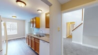 Located at 1921 Parkcrest Dr SW in Wyoming, Michigan, this two-story home offers three bedrooms, two bathrooms, and a practical, well-organized layout spread across two floors. The main floor encompasses the majority of the living space and features a galley-style kitchen equipped with warm oak cabinetry, granite-look countertops, a double stainless steel sink, and white appliances including a range, microwave, refrigerator, and dishwasher. Durable wood-look flooring runs throughout the kitchen, complementing the neutral color palette. The living room is generously sized with plush carpeting, a sliding glass door fitted with vertical blinds that opens to an outdoor balcony, and a wall-mounted air conditioning unit. Natural light filters in through the large sliding door, brightening the space. Both bathrooms feature oak vanities with granite-look countertops and mirrors; the full bath includes a shower-tub combo. The bedrooms are carpeted and well-lit with natural light from windows. A dedicated laundry closet on the upper floor houses a stacked washer and dryer unit alongside built-in shelving. Six-panel interior doors and clean white trim are consistent throughout, lending a cohesive, tidy aesthetic to the entire home.