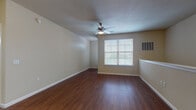 This single-floor residence is designed with an open, functional layout that connects the main living and kitchen areas seamlessly. The living room features rich, dark hardwood-style flooring, a ceiling fan with integrated lighting, and a large window fitted with blinds that allows natural light to fill the space. Neutral-toned walls and clean white baseboards contribute to a bright, welcoming ambiance throughout.

The kitchen is well-appointed with dark espresso cabinetry, granite-style countertops, and a full suite of black appliances including a refrigerator, electric range, built-in microwave, and dishwasher. A built-in wine rack adds a distinctive touch above the cabinetry, while pendant lighting and track lighting illuminate both the kitchen island and the workspace below.

The bedrooms are carpeted for comfort and each receives ample natural light through large windows with blinds. Ceiling fans provide additional airflow and comfort. The bathroom features hardwood-style flooring consistent with the main living areas, a full tiled tub-and-shower combination, a dark vanity with a granite-style countertop, and chrome fixtures throughout. The overall design is cohesive, practical, and move-in ready, offering a comfortable and well-equipped living environment.