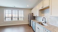 Located at 1550 Kenny Rd in Columbus, Ohio, this well-appointed single-floor residence offers a thoughtfully designed layout with modern finishes throughout. The kitchen is a standout feature, showcasing crisp white shaker cabinetry with matte black hardware, light granite countertops, a decorative tile backsplash, and a full suite of stainless steel appliances including a refrigerator with ice maker, dishwasher, microwave, and range. A undermount sink with a matte black faucet adds a refined touch, while a large window invites natural light into the space. Rich hardwood-style flooring flows seamlessly throughout the main living areas, complementing the neutral, warm-toned walls. The spacious living area benefits from abundant natural light through large windows with views of the surrounding neighborhood. A well-lit hallway connects the rooms and features a convenient in-unit stacked washer and dryer closet. The bathroom is elegantly finished with intricate hexagonal patterned tile flooring, subway-tiled walk-in shower enclosed by a glass door, a granite-top vanity, and matte black fixtures including a towel warmer. Recessed lighting throughout adds a clean, contemporary feel to every room in this move-in-ready residence.