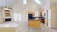Located at 5900 SW 76th Court in Gainesville, FL, this multi-story home spans three floors and offers a thoughtfully designed layout with two bedrooms, two bathrooms, and a versatile loft space. The main floor is the heart of the home, showcasing a dramatic vaulted ceiling that rises to an impressive height, flooding the open-concept kitchen and living area with natural light through a skylight and high clerestory windows. The kitchen features warm honey-toned cabinetry, dark granite countertops, a center island, and black appliances, including a French door refrigerator and built-in oven. The living area is anchored by a cozy fireplace with a built-in display nook above, a ceiling fan, and French doors that open to the outdoors. The main floor also includes a hallway and convenient access to the stairways. Upstairs, the loft offers flexible additional living space with a large window and staircase access. The bedrooms are carpeted and feature ceiling fans and walk-in closets with wire shelving. The bathrooms are finished with tile flooring. Throughout the home, neutral tones, plush carpeting, and an abundance of natural light create a warm and welcoming ambiance.