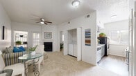 This well-designed single-floor residence offers a bright and welcoming layout that balances comfort and practicality. The living area serves as the heart of the home, featuring vaulted ceilings, soft wall-to-wall carpeting, and a ceiling fan that enhances air circulation. A fireplace anchors one wall, creating a cozy focal point, while a window with plantation shutters allows natural light to fill the space. A convenient in-unit laundry closet with a full-size washer and dryer is tucked neatly off the main living area, adding everyday functionality without sacrificing space. The kitchen is efficiently laid out with light cabinetry, a double stainless steel sink, a dishwasher, and a range, offering ample counter space for meal preparation. The bedroom is a restful retreat, finished with plush carpet flooring and a bright window dressed with white blinds and curtains, providing a calm and private atmosphere. The bathroom features wood-look flooring, a tub/shower combination clad in large-format gray tile, offering a clean and modern aesthetic. Throughout the residence, a neutral color palette, textured ceilings, and consistent finishes create a cohesive and inviting ambiance.