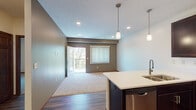 This single-floor residence offers a thoughtfully designed open-concept layout that seamlessly connects the kitchen and living areas. The kitchen is a standout feature, showcasing rich dark-wood cabinetry, white countertops, and a full suite of stainless steel appliances, including a range, microwave, dishwasher, and refrigerator. Pendant lighting hangs above a peninsula that provides additional prep space and casual seating, while wood-style flooring grounds the entire cooking and dining area.

The living space extends naturally from the kitchen, featuring neutral carpet, recessed lighting, and access to an outdoor balcony through a glass door. Vertical blinds on the windows allow for adjustable natural light and views of surrounding greenery.

The bedroom is generously proportioned, with plush carpet, a ceiling fan, and a large window fitted with vertical blinds. It connects directly to a spacious walk-in closet outfitted with built-in shelving and hanging rods, providing ample storage.

The bathroom is clean and functional, featuring a dark-wood vanity with a white countertop and sink, a large mirror, and a full tub-shower combination. Wood-style flooring and brushed nickel fixtures complete the polished, cohesive aesthetic found throughout the residence.
