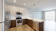 Located at 150 Main St in Longmont, Colorado, this well-appointed 2-bedroom, 1-bathroom residence offers a thoughtfully designed layout across a single floor. The open-concept kitchen and living area serves as the heart of the home, featuring stainless steel appliances, two-tone cabinetry with rich wood lower cabinets and crisp white uppers, a classic subway tile backsplash, and a sleek peninsula with a quartz countertop and an undermount sink. Recessed lighting and a modern linear pendant fixture illuminate the space, while wood-look vinyl plank flooring flows throughout the main living areas, adding warmth and continuity. A sliding barn door adds a distinctive architectural touch connecting spaces. The living area features a large sliding glass door with vertical blinds, allowing abundant natural light and outdoor views. Both bedrooms are carpeted for comfort, each equipped with a ceiling fan with light. The primary bedroom offers generous proportions and convenient access to an in-unit stacked washer and dryer. The bathroom is finished with wood-look tile floors, a wood-toned vanity with a white countertop, and a full tub-shower combination with large-format tile surround and a sliding glass door.