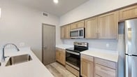 Located at 205 S Pines Rd in Spokane Valley, WA, this thoughtfully designed one-bedroom, one-bathroom residence offers a clean, modern aesthetic throughout its efficiently laid-out single floor. Light-toned luxury vinyl plank flooring runs through the main living areas, complementing the neutral wall palette and creating a bright, cohesive feel.

The kitchen is a standout feature, equipped with stainless steel appliances including a refrigerator, electric range, and over-the-range microwave. Light wood-tone shaker-style cabinetry pairs with crisp white countertops, providing ample storage and prep space. A peninsula counter extends the workspace and adds versatility for casual dining.

The living room is open and airy, highlighted by recessed lighting, a wall-mounted mini-split HVAC unit, and sliding glass doors that open onto a private balcony with views of the surrounding community — allowing natural light to fill the space.

The bedroom is comfortably sized and features carpet flooring, a wall-mounted mini-split unit, and direct access to a generous walk-in closet equipped with wire shelving and hanging rods for organized storage.

The bathroom is well-appointed with a light wood vanity, white countertop, a large mirror with overhead lighting, a tub-shower combination, and a tall storage cabinet, all finished with matching wood-tone details that tie the space together.