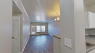 This single-story residence offers a practical and comfortable layout across two bedrooms and two bathrooms. The combined kitchen and living area forms the heart of the unit, where wood-look plank flooring extends throughout the main living spaces, complemented by neutral gray-toned walls and white crown molding. A small chandelier adds a refined touch above the dining area, while a broad set of windows and a glass-paneled door allow generous natural light to fill the living room.

The kitchen is configured as a peninsula layout, featuring white upper cabinetry, a dark countertop, and an electric range. A refrigerator is accessible just beyond the kitchen, keeping appliances centrally organized. Two hallways connect the living areas to the private quarters, with a dedicated closet providing additional storage.

Both bedrooms are carpeted and finished with neutral tones. The primary bedroom is a well-proportioned space with a ceiling fan and natural light from a side window. Each bedroom is served by its own full bathroom, both featuring tiled shower-tub combinations, wood-look flooring, vanity cabinetry with dark countertops, and white cabinetry for storage. The overall design is clean, consistent, and move-in ready.