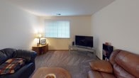 Located at 11200 W Cleveland Ave in West Allis, Wisconsin, this single-floor unit offers a well-organized layout designed for comfortable everyday living. The living room is generously sized, featuring neutral carpet flooring, large windows with blinds that bring in natural light, and an open sightline into the dining area, which is finished with a ceiling fan overhead. The galley-style kitchen is efficiently laid out with wood-toned cabinetry, dark laminate countertops, tile flooring, a double basin sink, and black appliances including a refrigerator and range. The unit includes two bedrooms. The primary bedroom features sliding glass doors with vertical blinds opening to an outdoor space with greenery views, along with carpeted flooring and ample room for a dresser and media setup. The second bedroom is bright and cozy, with a window dressed in sheer curtains and blinds, soft carpet, and generous closet access. Two bathrooms serve the unit — one with a wide vanity, large mirror, and bright vanity lighting, and a second full bathroom with a wood-cabinet vanity, tile flooring, and a shower-tub combination. Throughout the unit, neutral wall tones and consistent carpet and tile flooring create a cohesive, move-in ready environment.