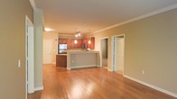 This single-floor residence offers a thoughtfully designed open-concept layout that seamlessly connects the main living areas, creating a sense of spaciousness and flow. The warm hardwood flooring extends throughout, anchoring the space with a sense of continuity and warmth.

The kitchen is a standout feature, showcasing rich medium-toned wood cabinetry that rises toward the ceiling, complemented by stainless steel appliances and a generous breakfast bar peninsula. Elegant pendant lighting hangs above the bar, providing both task lighting and a decorative touch, while a track lighting system overhead ensures the kitchen is well illuminated. The countertops offer ample workspace, making the kitchen as functional as it is visually appealing.

Crown molding runs along the ceiling throughout the living area, adding a refined architectural detail that elevates the overall aesthetic. The neutral wall tones create a versatile backdrop that pairs well with a variety of furnishing styles. Natural doorways lead to additional rooms, suggesting a practical and well-organized floor plan. The space is bathed in warm ambient lighting, contributing to an inviting and comfortable atmosphere ideal for both everyday living and entertaining.