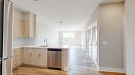 Located at 219 Ash Creek Boulevard in Fairfield, CT, this thoughtfully designed 2-bedroom, 1-bathroom residence offers a clean, modern aesthetic throughout its well-appointed single-floor layout. Light-toned hardwood flooring flows seamlessly across the entire living space, complementing the neutral warm-gray palette that unifies every room.

The open-concept kitchen is a standout feature, showcasing light wood cabinetry, a peninsula with a white quartz countertop, stainless steel appliances including a refrigerator, range, microwave, and dishwasher, and recessed lighting overhead. The kitchen opens directly into the living room, creating a bright, connected living and dining area bathed in natural light from large windows.

Both bedrooms are well-proportioned, with the primary bedroom offering ample space and access to the private balcony. The balcony presents a stunning panoramic view of Ash Creek, with lush greenery and open water stretching beneath a wide-open sky. Two closets provide convenient storage throughout the unit.

The bathroom features tile flooring, a light wood vanity with white countertop, a mirror with overhead lighting, and marble-tiled shower and tub surround. An in-unit laundry area adds everyday practicality to this move-in-ready residence.