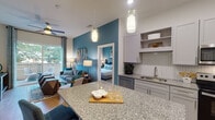 Located at 305 Oberlin Rd in Raleigh, NC, this single-floor residence combines contemporary design with functional living. The open-concept layout connects the kitchen and living area seamlessly, creating an inviting and cohesive space. The kitchen is equipped with stainless steel appliances, including a side-by-side refrigerator, electric range, and built-in microwave. Crisp white shaker cabinetry, granite countertops, and a herringbone tile backsplash lend a polished aesthetic, while a large granite-topped island with seating serves as a central gathering point. Pendant lighting above the island adds a warm, modern touch. Hardwood-style flooring runs throughout the main living areas, complementing the neutral palette. The living room features a bold teal accent wall, ceiling fan, and sliding glass doors that open to a private balcony with outdoor seating and a lush tree-lined view. Both bedrooms are carpeted and offer a calm retreat, each accented with a teal feature wall. The primary bedroom connects to a bathroom with granite vanity countertops and a glass-enclosed walk-in shower with white subway tile surround. A second full bathroom also features granite counters and refined fixtures. A dedicated laundry area and ample storage complete this well-designed residence.