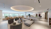 Located at 320 W South St in downtown Raleigh, NC, this elegantly designed single-floor space offers a seamless blend of modern aesthetics and functional comfort across a generously sized footprint. The interior is unified by polished concrete floors, soft neutral tones, and warm wood accents that carry throughout each area.

The main lounge is a standout feature, showcasing a wood-paneled ceiling with integrated LED lighting, a backlit tile accent wall, and a curved sectional seating arrangement complemented by an assortment of sleek occasional chairs and small round tables. Floor-to-ceiling windows flood the space with natural light and frame sweeping views of the Raleigh skyline.

The adjoining dining room seats a large group at a substantial natural wood table, set beneath a cluster of contemporary globe pendant lights. Large-scale navy artwork and lush indoor plants lend the room a refined yet welcoming atmosphere. The open kitchen features a curved island with rich marble-look countertops, handleless cabinetry in a muted blue-grey finish, and professional-grade appliances.

The hallway provides smooth connectivity between spaces, while the expansive outdoor terrace offers breathtaking panoramic views of downtown Raleigh. The terrace is outfitted with generous lounge seating, glass balustrades, and wood-lined ceiling overhangs, making it an exceptional setting for gatherings or relaxation.